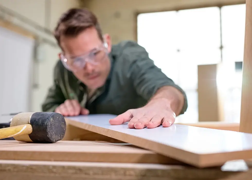 Schreiner prüft Holzbrett Tischler überprüft die Arbeit, nachdem er Holz mit Schutzfarbe behandelt und poliert hat. Tischlerei, hart bei der Arbeit, Qualitätskontrolle, Heimwerken, Do-it-yourself-Konzept. Fokus auf Händen und Brett.